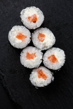 Siyah arka planda somon balıklı Maki Suşi Rolls. Suşi menüsü. Japon yemeği. Sushi dürümlü lezzetli Japon yemeklerini yakından çek. Dikey fotoğraf