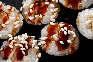 Maki suşi ruloları, siyah arka planda siyah kayanın üzerinde yılan balığı. Suşi menüsü. Japon yemeği. Sushi dürümlü lezzetli Japon yemeklerini yakından çek. Yatay fotoğraf
