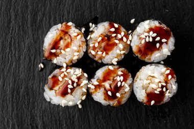 Maki suşi ruloları, siyah arka planda siyah kayanın üzerinde yılan balığı. Suşi menüsü. Japon yemeği. Sushi dürümlü lezzetli Japon yemeklerini yakından çek. Yatay fotoğraf