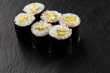 Salatalıklı Maki Suşi Rolls ya da siyah arka planda siyah taşlı avokado. Suşi menüsü. Japon yemeği. Sushi dürümlü lezzetli Japon yemeklerini yakından çek. Yatay fotoğraf