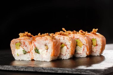 İçinde avokado, karides, yeşil soğan, alevli somon ve krem peynirli suşi rulosu ve siyah tahtada kızarmış soğan var. Philadelphia usulü suşi ve karides. Suşi menüsü. Yatay fotoğraf.