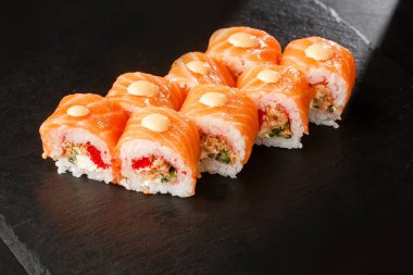 Uçan balık havyarlı suşi ruloları, kızarmış soğan, somon ve krem peyniri içinde ve siyah tahtada izole. Philadelphia usulü suşi ve karides. Suşi menüsü. Yatay fotoğraf.