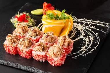 İçinde avokado, yılan balığı, salatalık ve krem peynirli suşi rulosu ve siyah tahtada ton balığı sosu var. Kaliforniya dürümleri turuncu tobiko ya da masago havyarı ile kaplıdır. Suşi menüsü. Yatay fotoğraf.