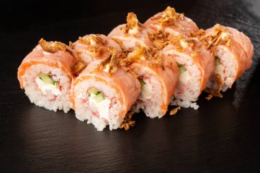 İçinde salatalık, karides, yengeç eti, alevli somon ve krem peynirli suşi ruloları ve siyah tahtada kızarmış soğan var. Philadelphia suşisi ve alevli somon. Suşi menüsü. Yatay