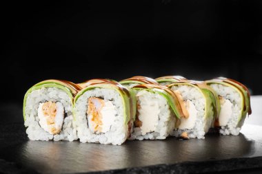 İçinde ızgara tempura, avokado, omlet ve krem peynirli suşi ruloları var. Philadelphia, siyah arka planda tempura karidesli. Suşi menüsü. Japon yemeği. Yatay fotoğraf.