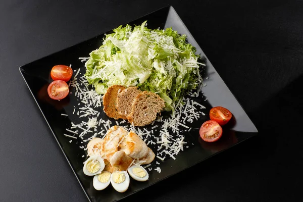 Chicken Salad. Chicken Caesar Salad. Caesar Salad with grilled chicken on plate. Grilled chicken breasts, tomatoes, fresh salad in plate. On black background. Horizontal photo.