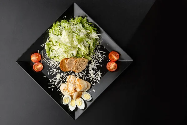 Chicken Salad. Chicken Caesar Salad. Caesar Salad with grilled chicken on plate. Grilled chicken breasts, tomatoes, fresh salad in plate. On black background. Horizontal photo.