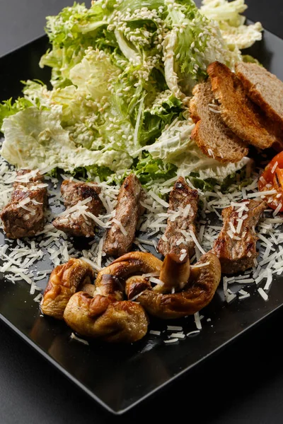 Veal salad with cherry tomatoes, mushrooms on a black plate on dark background. Plate on dark background, copy space. Restaurant food, close up. Meat salad. Vertical photo. — ストック写真