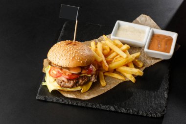 Siyah arka planda izole edilmiş patates kızartmalı büyük bir çizburger. Köfteli hamburger, soğan, domates, marul turşusu, yıllanmış çedar, hardal, domates reçeli, mayonez. Yatay