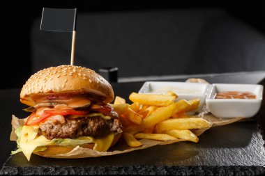 Siyah arka planda izole edilmiş patates kızartmalı büyük bir çizburger. Köfteli hamburger, soğan, domates, marul turşusu, yıllanmış çedar, hardal, domates reçeli, mayonez. Yatay