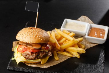 Siyah arka planda izole edilmiş patates kızartmalı büyük bir çizburger. Köfteli hamburger, soğan, domates, marul turşusu, yıllanmış çedar, hardal, domates reçeli, mayonez. Yatay
