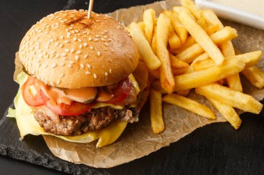 Siyah arka planda izole edilmiş patates kızartmalı büyük bir çizburger. Köfteli hamburger, soğan, domates, marul turşusu, yıllanmış çedar, hardal, domates reçeli, mayonez. Yatay