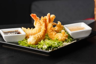 Tempura Koyu Kızarmış Karides Ebi, acı biberli ve soya soslu, siyah tahta taşlı, siyah arka planda. Japon yemek tarzı aperatif. Kızarmış karidesi yakından çiftleştirmek. Yatay fotoğraf.