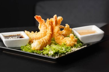 Tempura Koyu Kızarmış Karides Ebi, acı biberli ve soya soslu, siyah tahta taşlı, siyah arka planda. Japon yemek tarzı aperatif. Kızarmış karidesi yakından çiftleştirmek. Yatay fotoğraf.