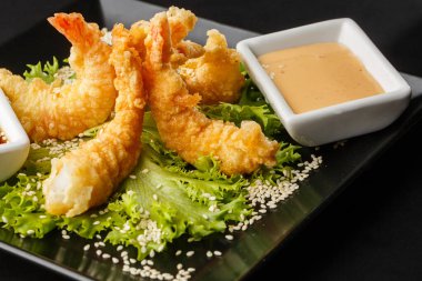 Tempura Koyu Kızarmış Karides Ebi, acı biberli ve soya soslu, siyah tahta taşlı, siyah arka planda. Japon yemek tarzı aperatif. Kızarmış karidesi yakından çiftleştirmek. Yatay fotoğraf.