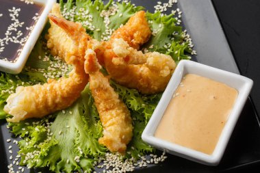 Tempura Koyu Kızarmış Karides Ebi, acı biberli ve soya soslu, siyah tahta taşlı, siyah arka planda. Japon yemek tarzı aperatif. Kızarmış karidesi yakından çiftleştirmek. Yatay fotoğraf.