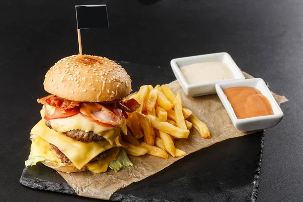 Big double cheeseburger with french fries isolated on black background. hamburger with beef patty , bacon, onion, tomato, lettuce pickles, aged cheddar, mustards, tomato jam, mayo. Horizontal