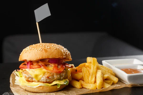 Big single chickenburger with french fries isolated on black background. hamburger with chicken patty , onion, tomato, lettuce pickles, aged cheddar, mustards, tomato jam, mayo. Horizontal