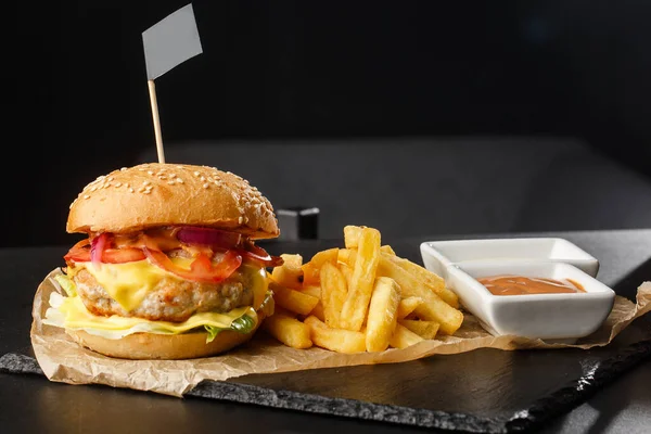Big single chickenburger with french fries isolated on black background. hamburger with chicken patty , onion, tomato, lettuce pickles, aged cheddar, mustards, tomato jam, mayo. Horizontal