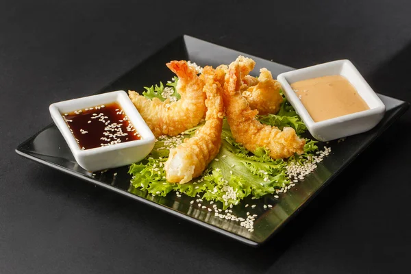 Tempura Koyu Kızarmış Karides Ebi, acı biberli ve soya soslu, siyah tahta taşlı, siyah arka planda. Japon yemek tarzı aperatif. Kızarmış karidesi yakından çiftleştirmek. Yatay fotoğraf.