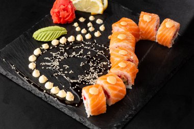 Somon, avokado, uçan balık havyarı, ton balığı ve krem peynirli suşi ruloları siyah tahtada izole. Somonlu Philadelphia suşisi. Suşi menüsü. Yatay fotoğraf.