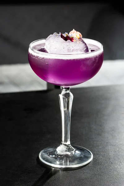 Cocktail Purple fatto in casa con un grande cubetto di ghiaccio su sfondo nero. Primo piano di cocktail viola in un bicchiere di margarita con bordi di zucchero, viola e schiuma proteica. Foto verticale . — Foto Stock