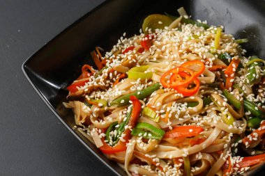 Sebzeli tavuk erişte kasesi. Udon kızarmış şehriye ile tavuk eti ve susam kasede koyu taş arka planda fotokopi alanı. Tavuk ve sebzeli spagetti makarna. Yatay fotoğraf.