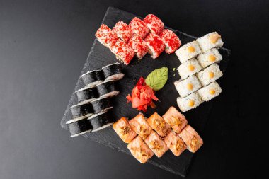 Siyah arka planda servis edilen çeşitli suşiler. Japon yemeği için suşi menüsü. Japon suşi seti. Ton balığı, somon, karides, yengeç, havyar ve avokado. Yatay fotoğraf.