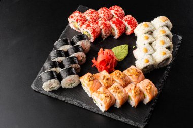 Siyah arka planda servis edilen çeşitli suşiler. Japon yemeği için suşi menüsü. Japon suşi seti. Ton balığı, somon, karides, yengeç, havyar ve avokado. Yatay fotoğraf.