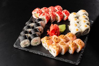 Siyah arka planda servis edilen çeşitli suşiler. Japon yemeği için suşi menüsü. Japon suşi seti. Ton balığı, somon, karides, yengeç, havyar ve avokado. Yatay fotoğraf.