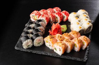 Siyah arka planda servis edilen çeşitli suşiler. Japon yemeği için suşi menüsü. Japon suşi seti. Ton balığı, somon, karides, yengeç, havyar ve avokado. Yatay fotoğraf.