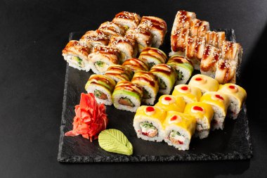 Siyah arka planda servis edilen çeşitli suşiler. Japon yemeği için suşi menüsü. Japon suşi seti. İçinde yılan balığı, karides, yengeç, havyar, Amerikan peyniri ve avokado var. Yatay fotoğraf.