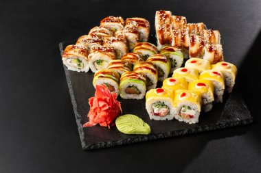 Siyah arka planda servis edilen çeşitli suşiler. Japon yemeği için suşi menüsü. Japon suşi seti. İçinde yılan balığı, karides, yengeç, havyar, Amerikan peyniri ve avokado var. Yatay fotoğraf.