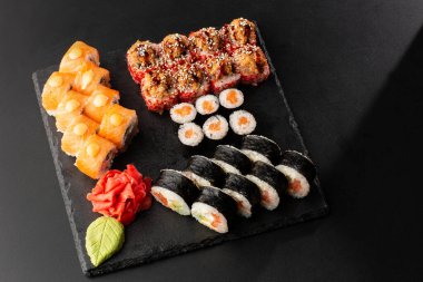 Siyah arka planda servis edilen çeşitli suşiler. Japon yemeği için suşi menüsü. Japon suşi seti. Ton balığı, somon, karides, yengeç ve avokado. Yatay fotoğraf.