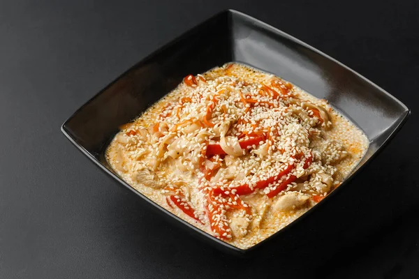 Hicken with vegetables and udon noodles in a delicate creamy cheese sauce in a black bowl on a black background. Horizontal photo. — Stock Photo, Image