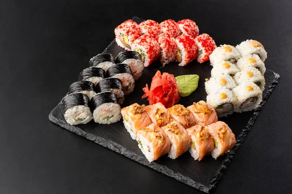 Siyah arka planda servis edilen çeşitli suşiler. Japon yemeği için suşi menüsü. Japon suşi seti. Ton balığı, somon, karides, yengeç, havyar ve avokado. Yatay fotoğraf.