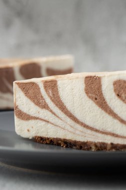 Süzme peynirli ev yapımı çikolatalı kek. Zebra mermer pastası. Lezzetli bir kahvaltı. Gri tabakta bir parça kek, beyaz mermer arka planda beyaz bardak. Seçici odaklanma. Dikey fotoğraf.