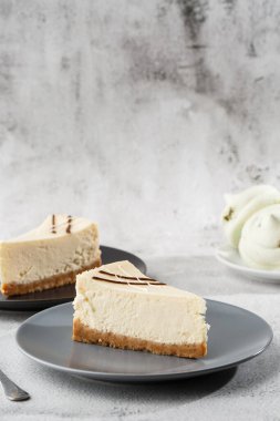 Cheesecake New York ya da beyaz masada bir fincan kahveli klasik cheesecake. Yakından bak. Lezzetli bir kahvaltı. Siyah tabakta bir parça kek, beyaz mermer arka planda beyaz bardak. Dikey fotoğraf.