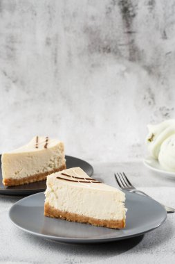 Cheesecake New York ya da beyaz masada bir fincan kahveli klasik cheesecake. Yakından bak. Lezzetli bir kahvaltı. Siyah tabakta bir parça kek, beyaz mermer arka planda beyaz bardak. Dikey fotoğraf.