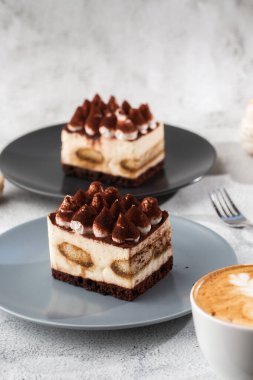 Tiramisu, mascarpone ve kahveli klasik tatlı. Hafif mermer arka planda koyu bir tabakta nefis bir Tiramisu keki. Dikey fotoğraf.
