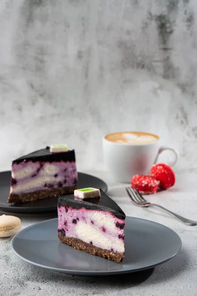 Böğürtlenli cheesecake ve beyaz masa üzerinde bir fincan kahve. Yakından bak. Lezzetli bir kahvaltı. Siyah tabakta bir parça kek, beyaz mermer arka planda beyaz bardak. Dikey fotoğraf.