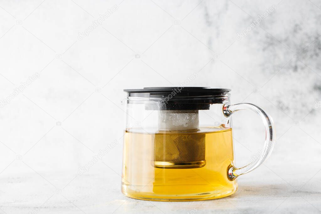 Glass teapot of green, camomile, chamomile or yellow tea isolated on bright marble background. Overhead view, copy space. Advertising for cafe menu. Coffee shop menu. Horizontal photo.