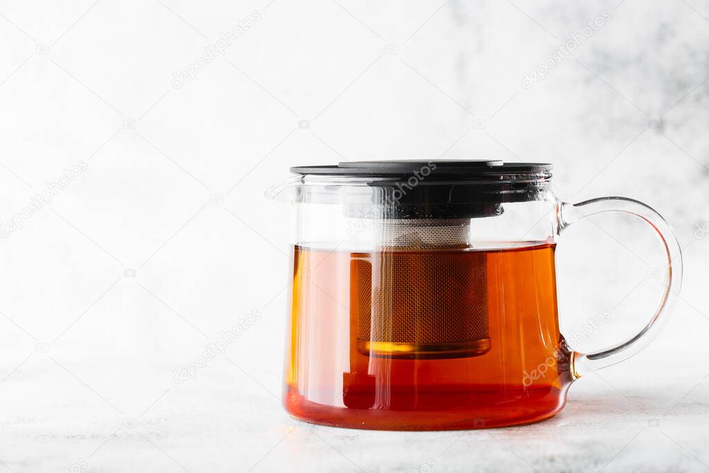 Glass teapot with black tea isolated on bright marble background. Overhead view, copy space. Advertising for cafe menu. Coffee shop menu. Horizontal photo.