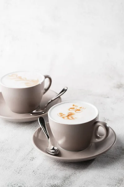 Due tazze bianche di caffè latte caldo con bella schiuma di latte latte texture art isolato su sfondo di marmo luminoso. Vista aerea, copiare spazio. Pubblicità per il menu del caffè. Menù della caffetteria. Fo verticale — Foto Stock
