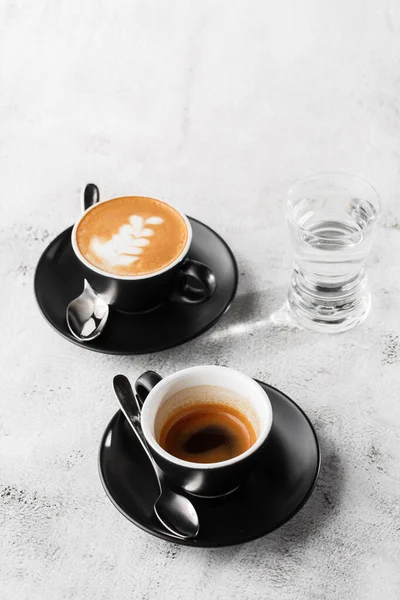 Duas xícaras escuras de café preto quente, café expresso, cappuccino com leite isolado em fundo de mármore brilhante. Visão geral, espaço de cópia. Publicidade para menu de café. Menu da cafetaria. Foto vertical . — Fotografia de Stock