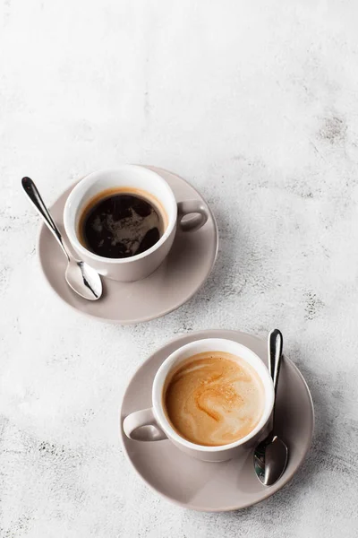 Två vita koppar varmt svart kaffe med mjölk isolerad på ljus marmor bakgrund. Overhead view, kopiera utrymme. Reklam för cafémenyn. Kafémenyn. Vertikalt foto. — Stockfoto