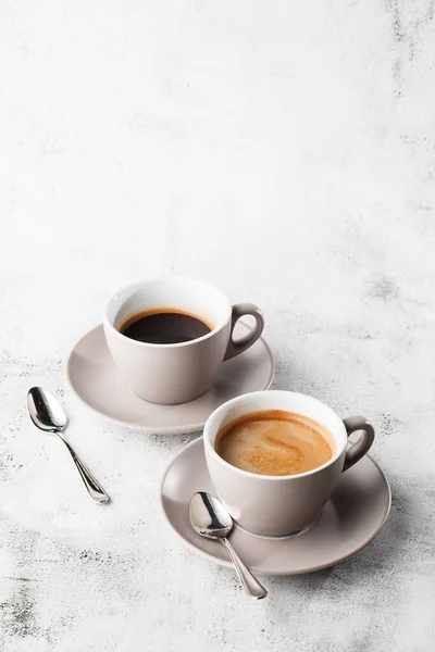 Två vita koppar varmt svart kaffe med mjölk isolerad på ljus marmor bakgrund. Overhead view, kopiera utrymme. Reklam för cafémenyn. Kafémenyn. Vertikalt foto. — Stockfoto