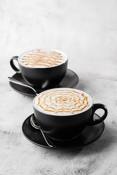Duas xícaras escuras de café com leite caramelo latte art textura isolada sobre fundo de mármore brilhante. Visão geral, espaço de cópia. Publicidade para menu de café. Menu da cafetaria. Foto vertical . — Fotografia de Stock