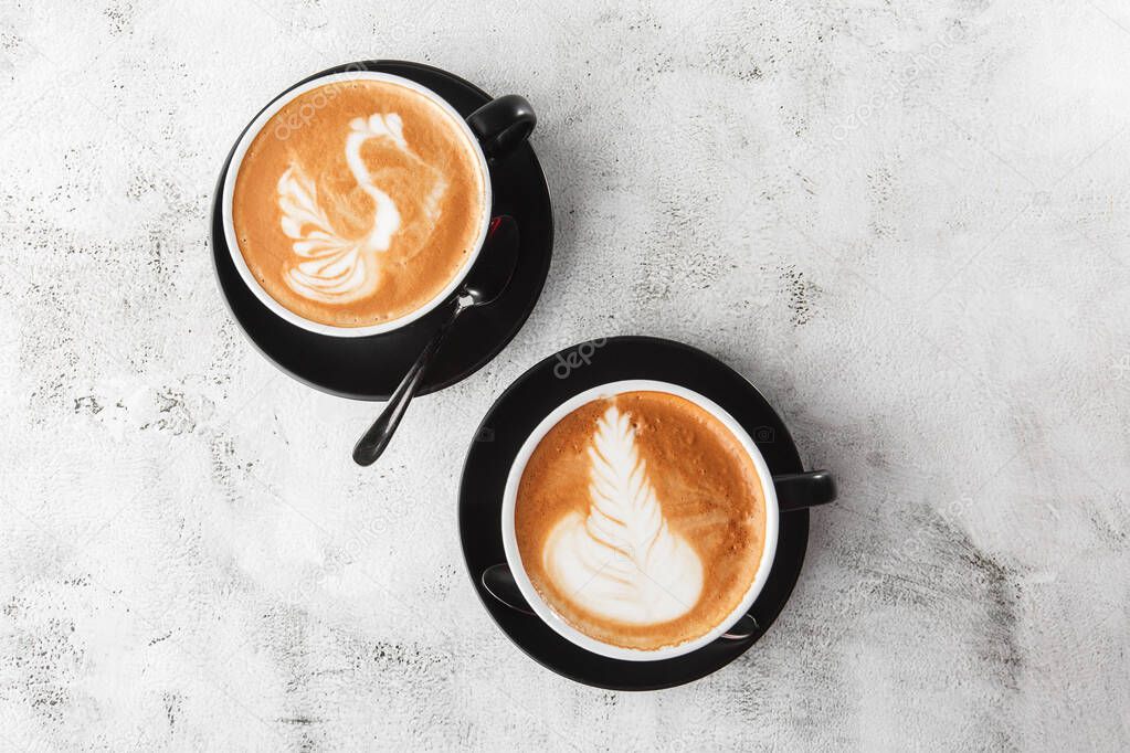 Two black cups of hot latte coffee with beautiful milk foam latte art texture isolated on bright marble background. Overhead view, copy space. Advertising for cafe menu. Coffee shop menu. Horizontal p