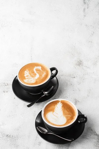 Duas xícaras pretas de café quente com latte de espuma de leite bonito textura arte latte isolado em fundo de mármore brilhante. Visão geral, espaço de cópia. Publicidade para menu de café. Menu da cafetaria. Pho vertical — Fotografia de Stock